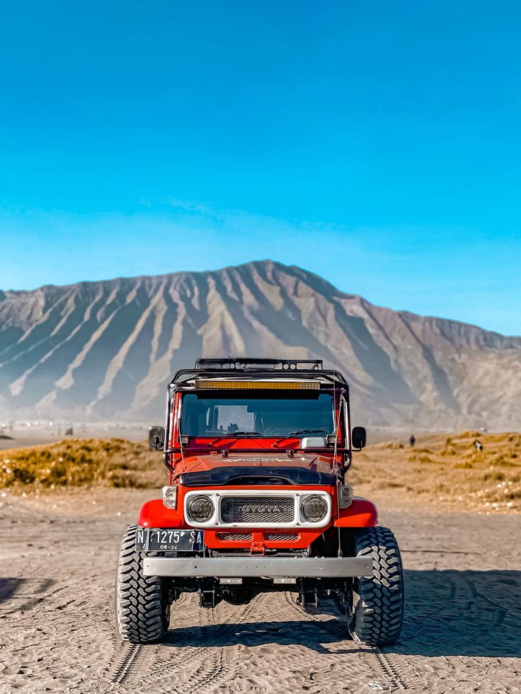 Jeep wisata melintasi lautan pasir Gunung Bromo dengan latar pegunungan Tengger