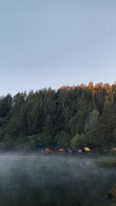 Danau Ranu Kumbolo dengan pantulan langit biru dan tenda pendaki di tepi sabana