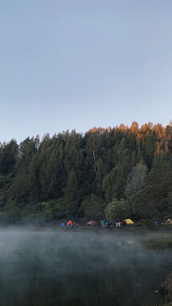 Danau Ranu Kumbolo dengan pantulan langit biru dan tenda pendaki di tepi sabana