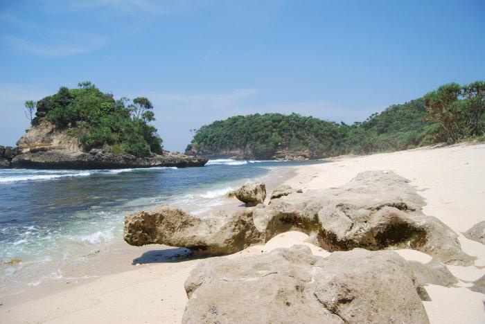 Hamparan pasir coklat bersih di Pantai Jonggring Saloko Malang dengan tebing karang menjulang dan ombak besar khas pantai selatan