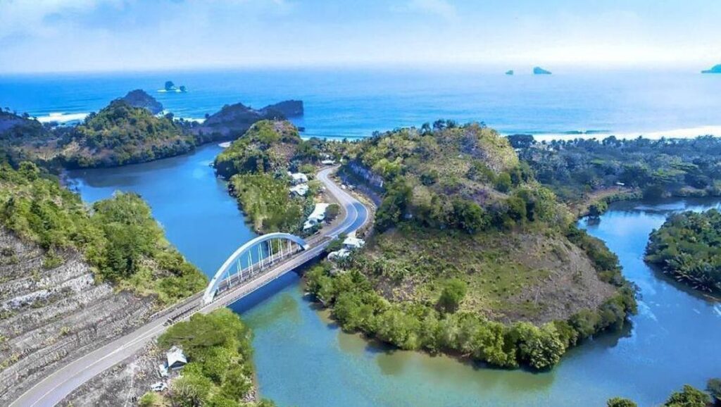 Jembatan Bajulmati di atas pasir cokelat kehitaman dengan ombak besar di latar belakang